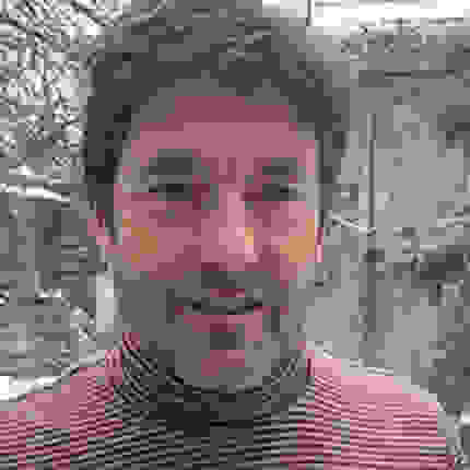 A portrait of Peter Garfield outside in a snowy yeard, wearing a pink and black striped turtleneck sweater