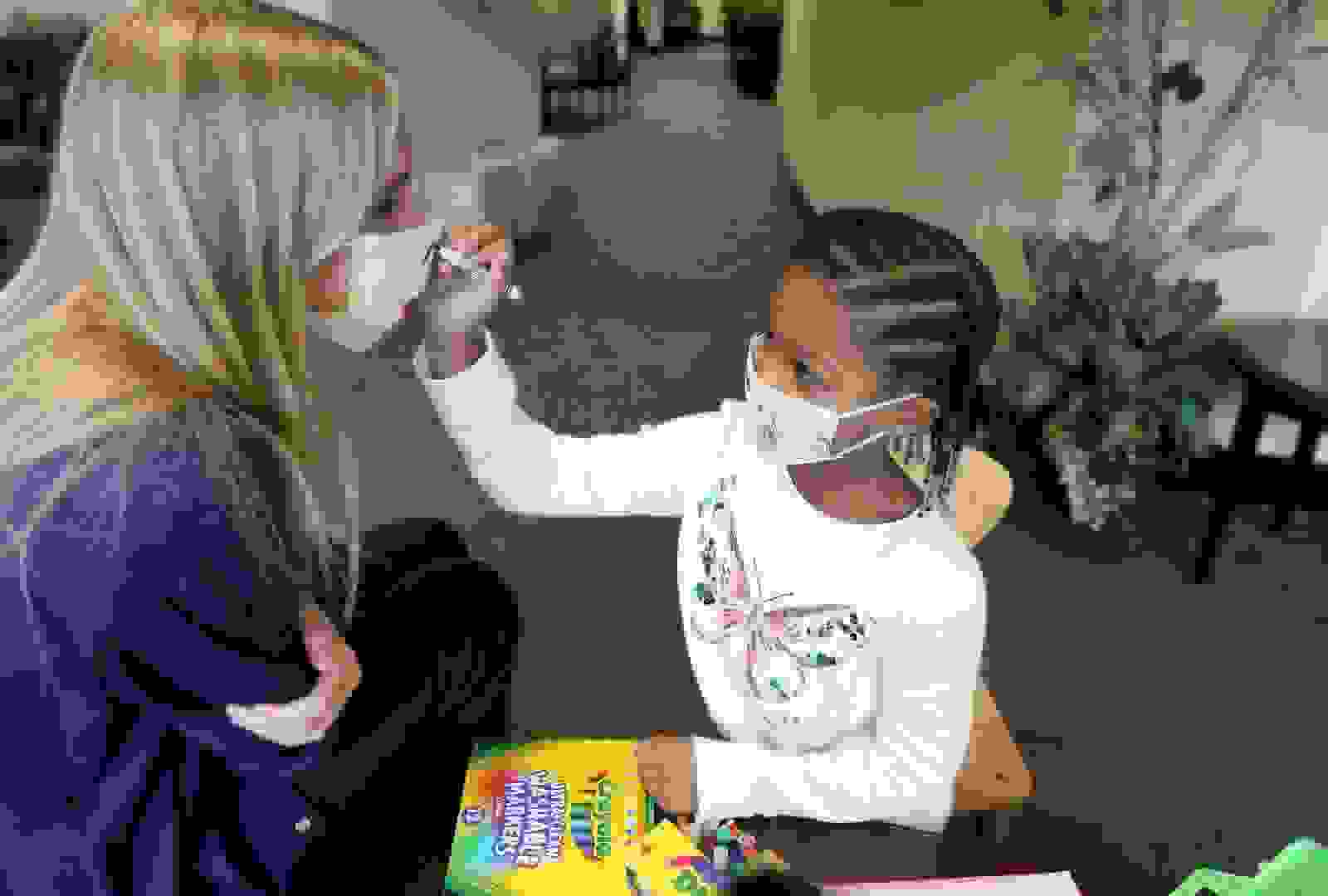 Child painting with markers on a face mask worn by a therapist