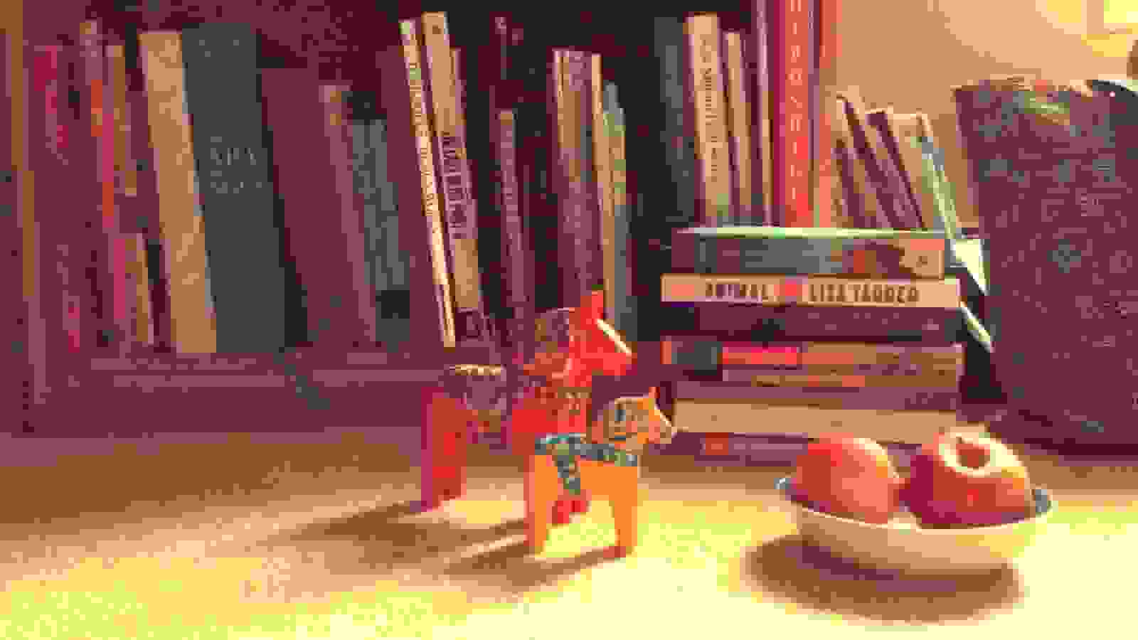 Here is a film still of two horse figurines standing in front of a row of books.