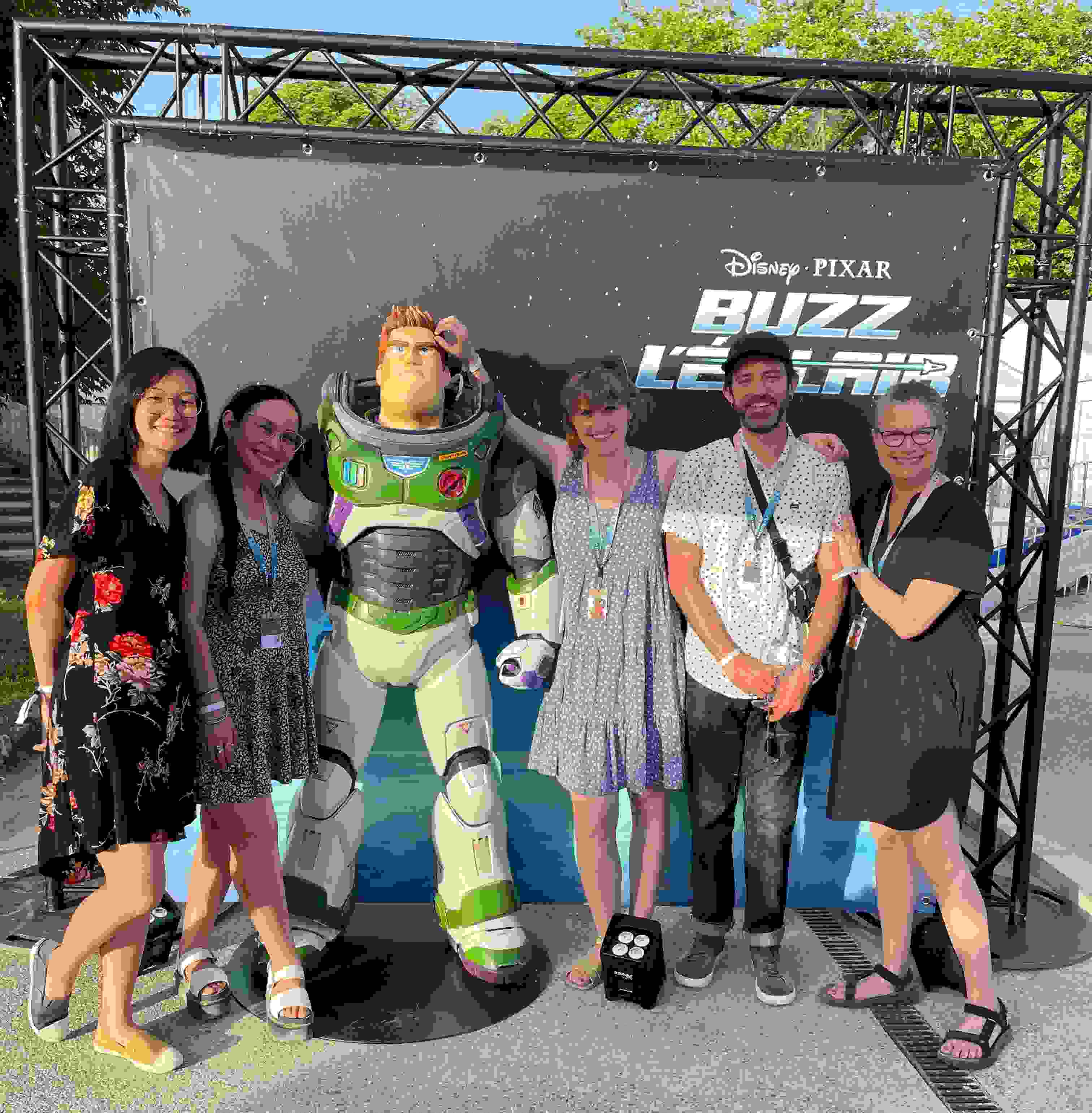 A photograph of people posing in front of a human-sized Buzz Lightyear figurine.