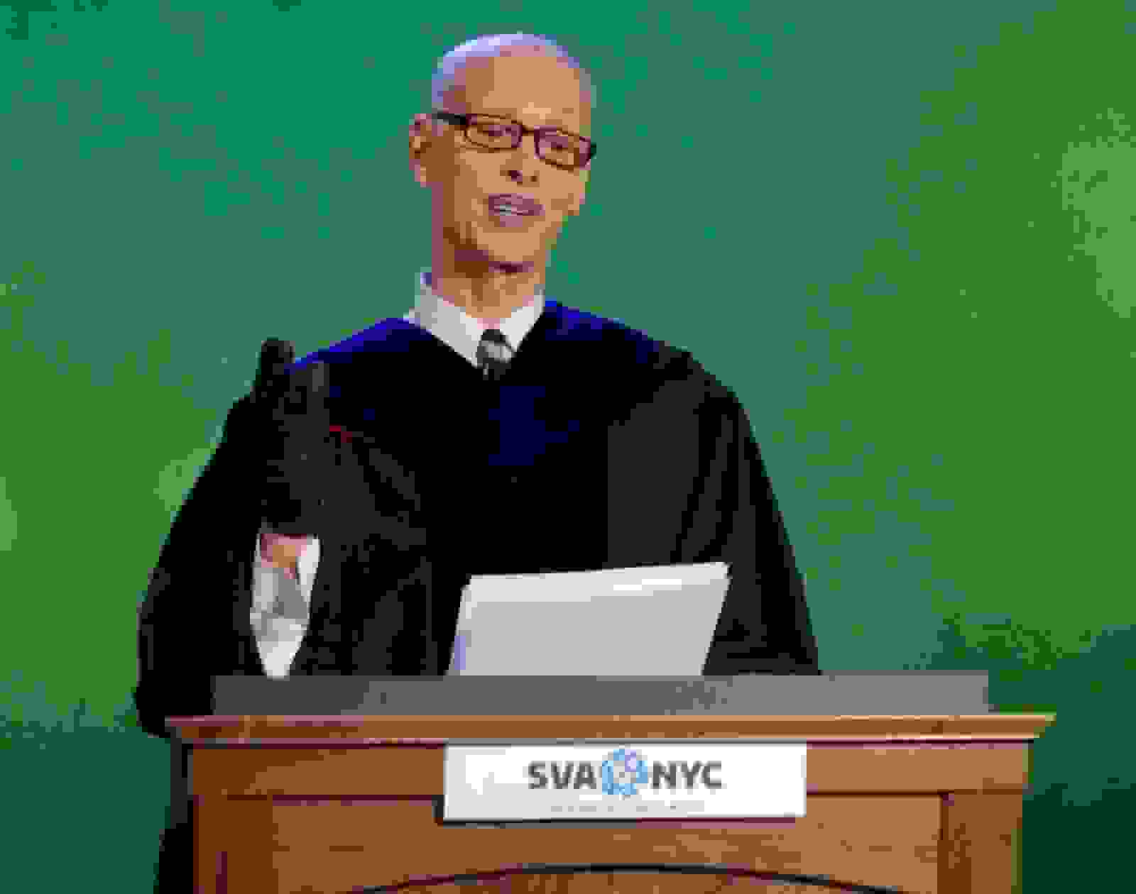 A photo of a man in a tie and graduation gown, standing at a podium set in front of a green screen.