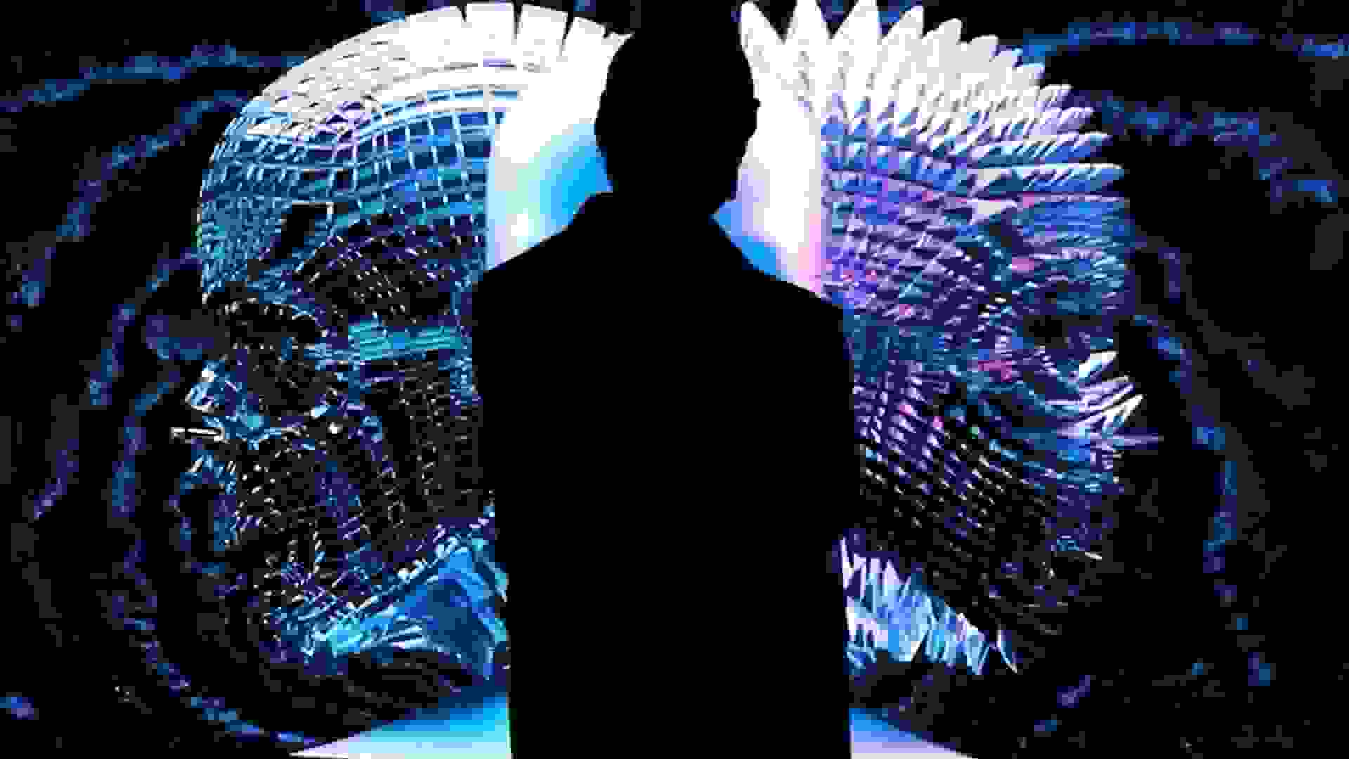 A silhouette of a person standing in front of a video projection of two abstract heads. 