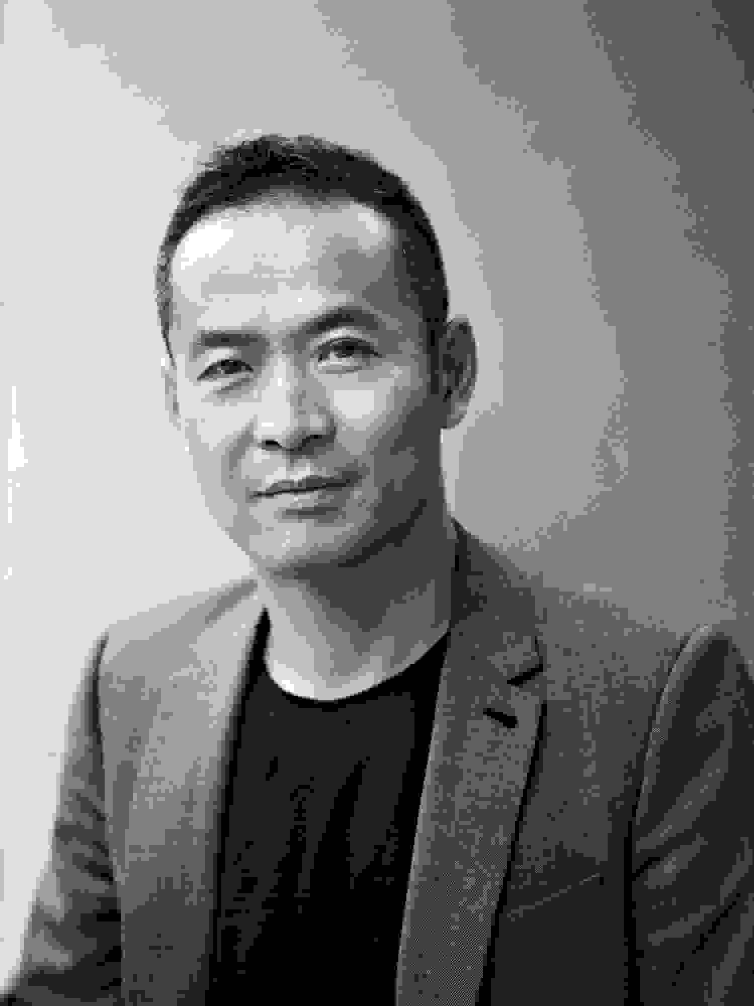 A black and white photograph of curator, ZHANG Ga. Zhang is an asian male wearing a black t-shirt and a suit jacket.