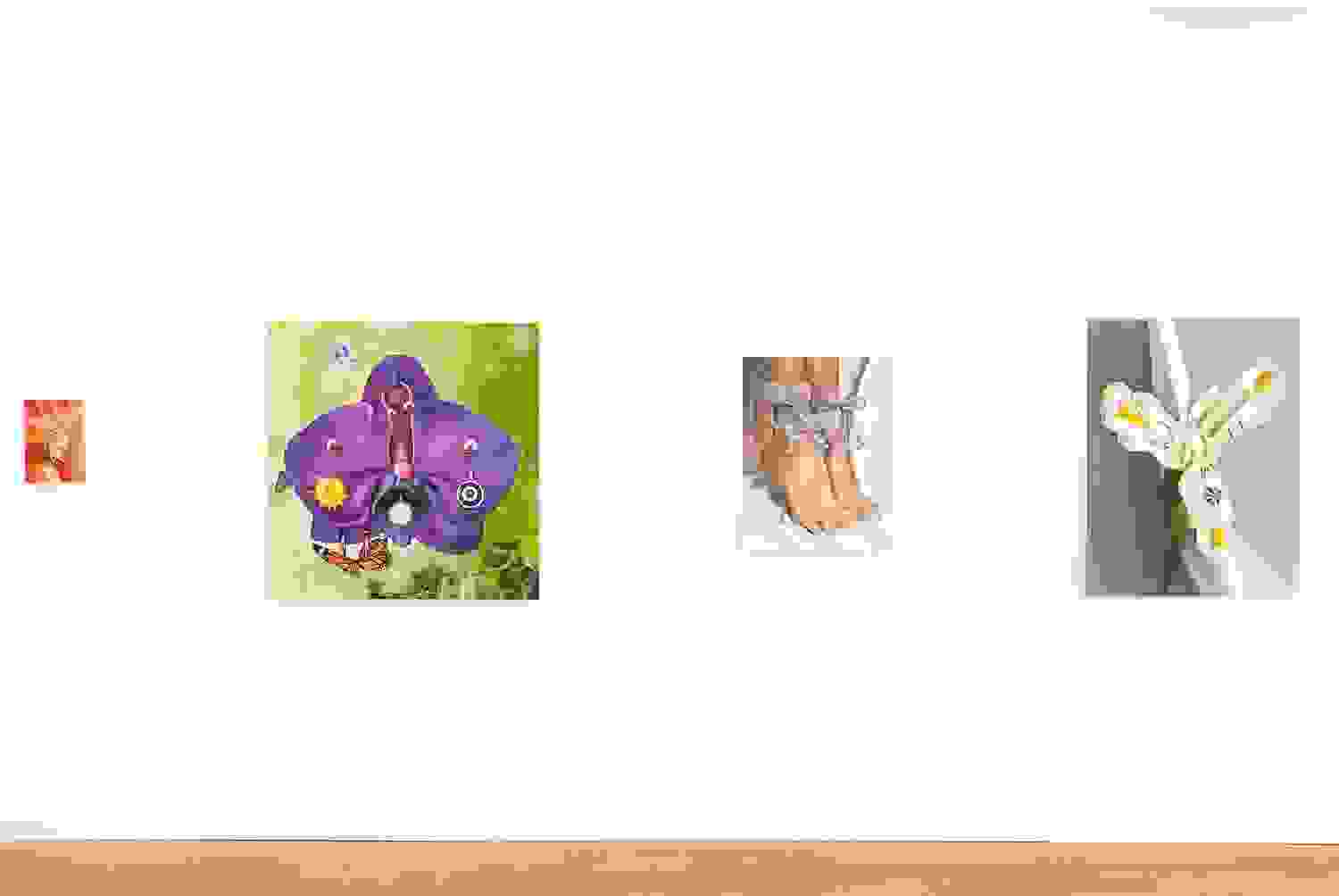 A wall of 4 paintings. Left to right: a small painting of a flower, a larger painting of a purple flower pierced with jewelry, a painting of feet, and a painting of another flower that has been pierced.  