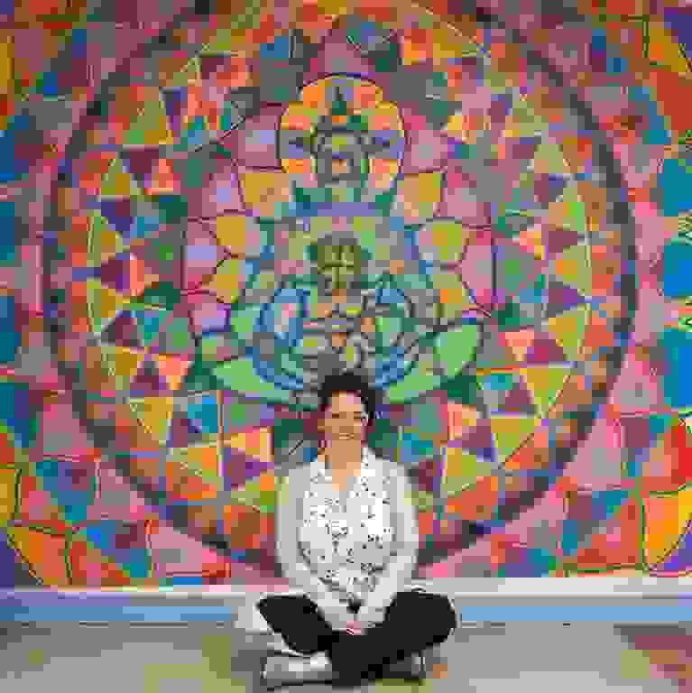 A woman sits in front of a colorful mural.