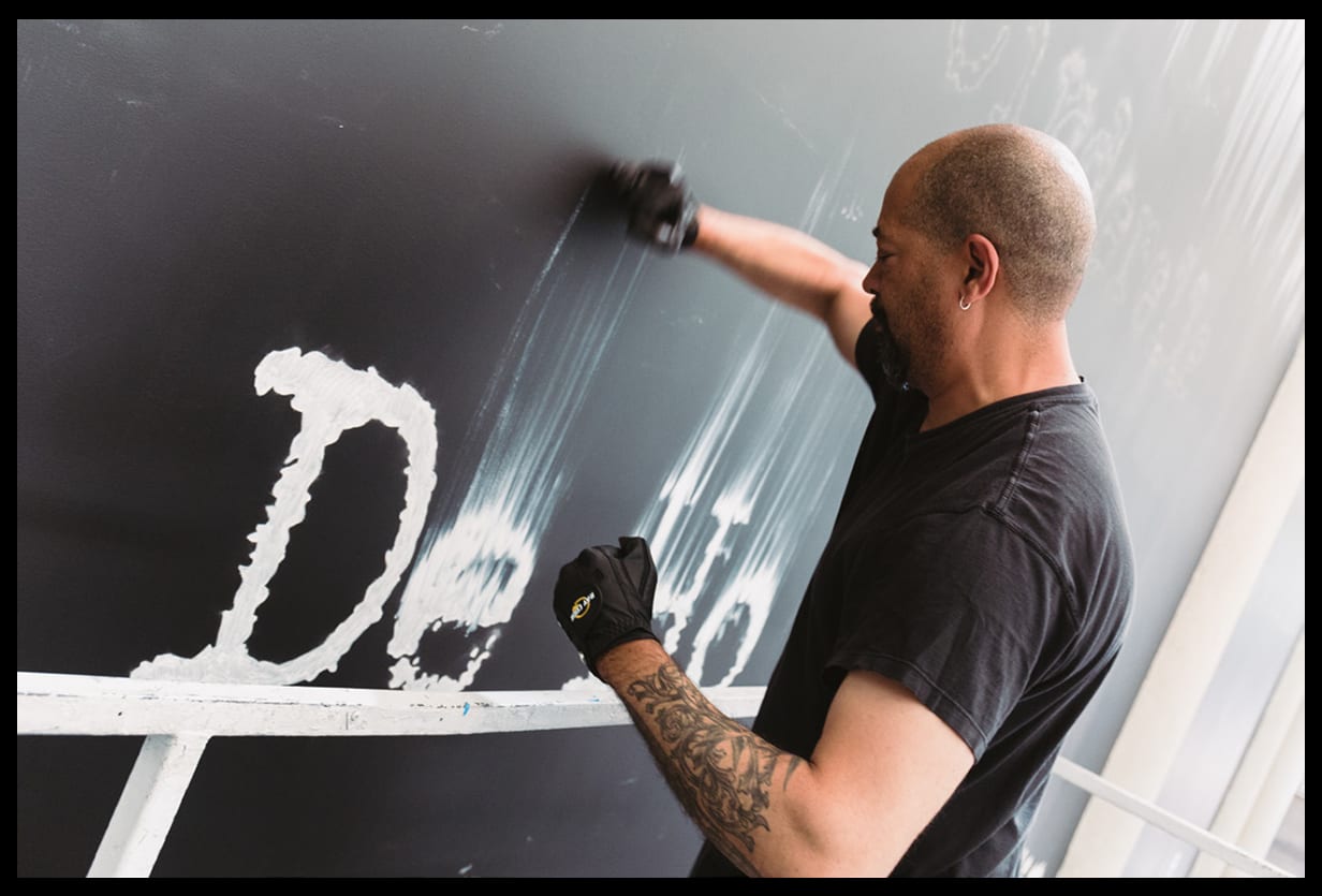 <p "="">Artist Gary Simmons uses his fists to smudge the wet paint of white letters on a black wall.
